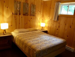 Una stanza in legno con un letto, due lampade da comodino e una finestra con tenda.
