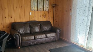 A room with a brown leather sofa, wooden walls, a floor lamp, and a window with a patterned curtain.