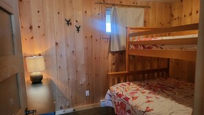 A bunk bed with a floral bedspread, a wooden desk with a lamp, and a window with a curtain.