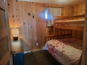 Un lit superposé avec une couvre-lit à motifs floraux, un bureau en bois avec une lampe et une fenêtre avec un rideau.
