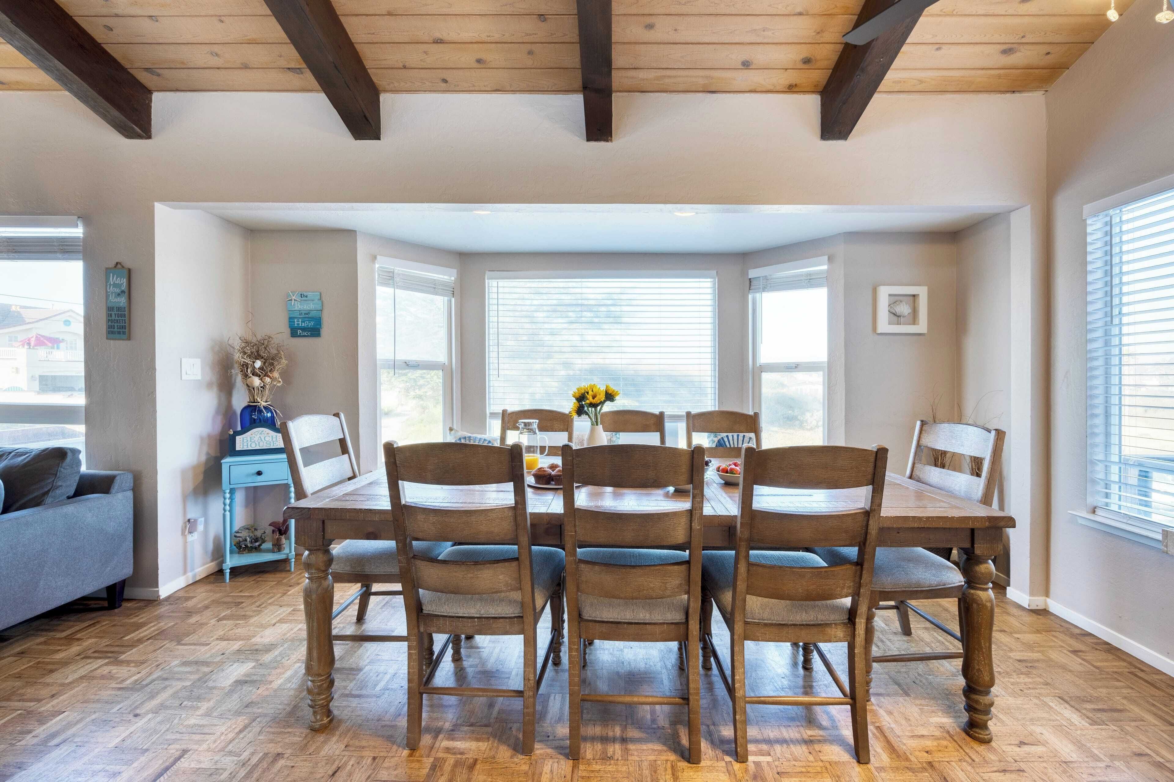 A dining area with a wooden table and chairs, a window with blinds, and a small side table with a vase.
