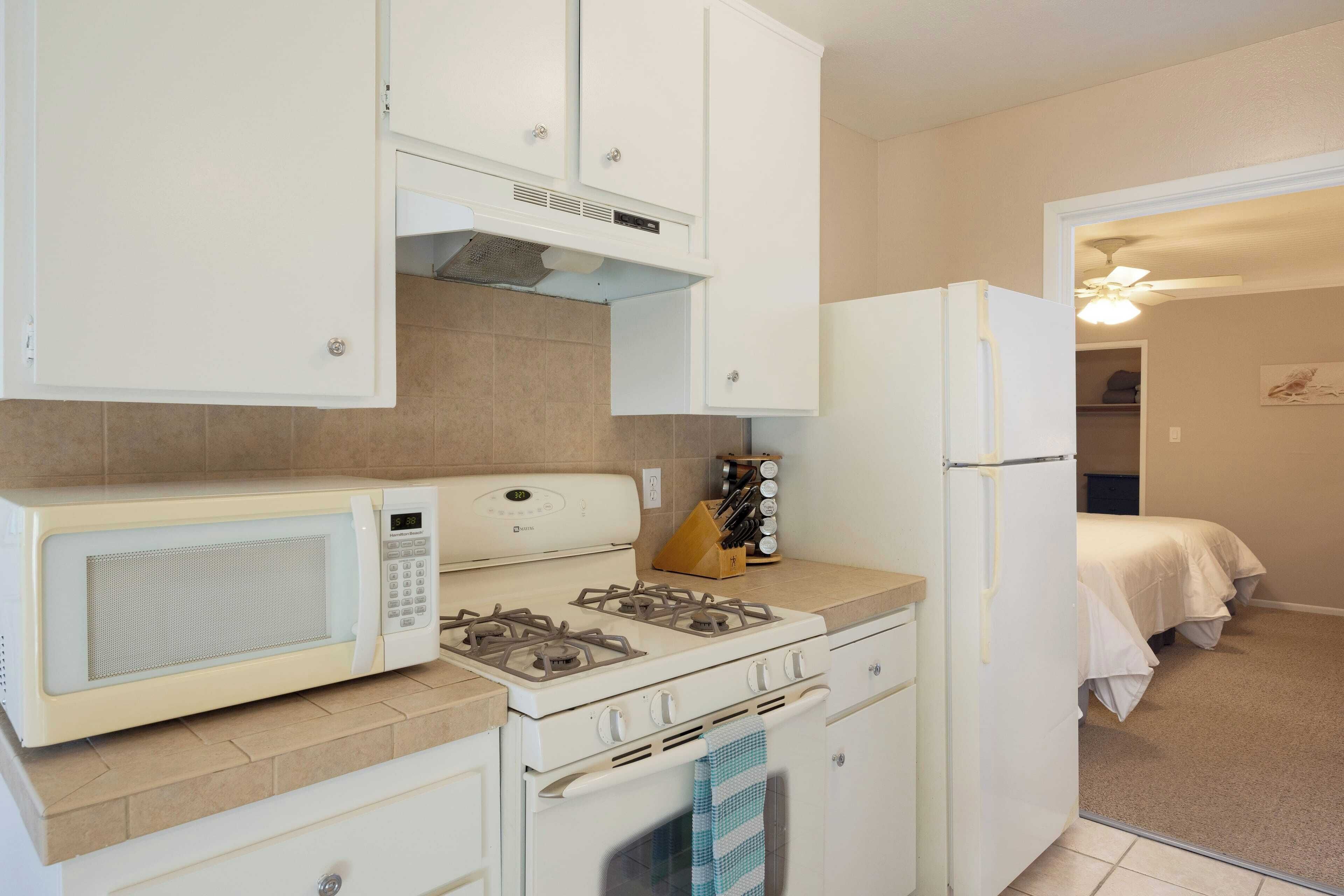 Une cuisine de taille réduite, dotée d’appareils électroménagers blancs, notamment un four à micro-ondes, une cuisinière et un réfrigérateur.