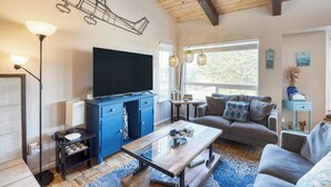 A modern living room with a flat-screen TV, blue cabinets, a sofa, and a coffee table. - Steps to Beach w/ Patio+deck Foosball Happy Bottom Beach House by Avantstay (Oceano)