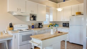 Una cocina con armarios blancos, estufa, microondas e isla de madera con un jarrón de flores.