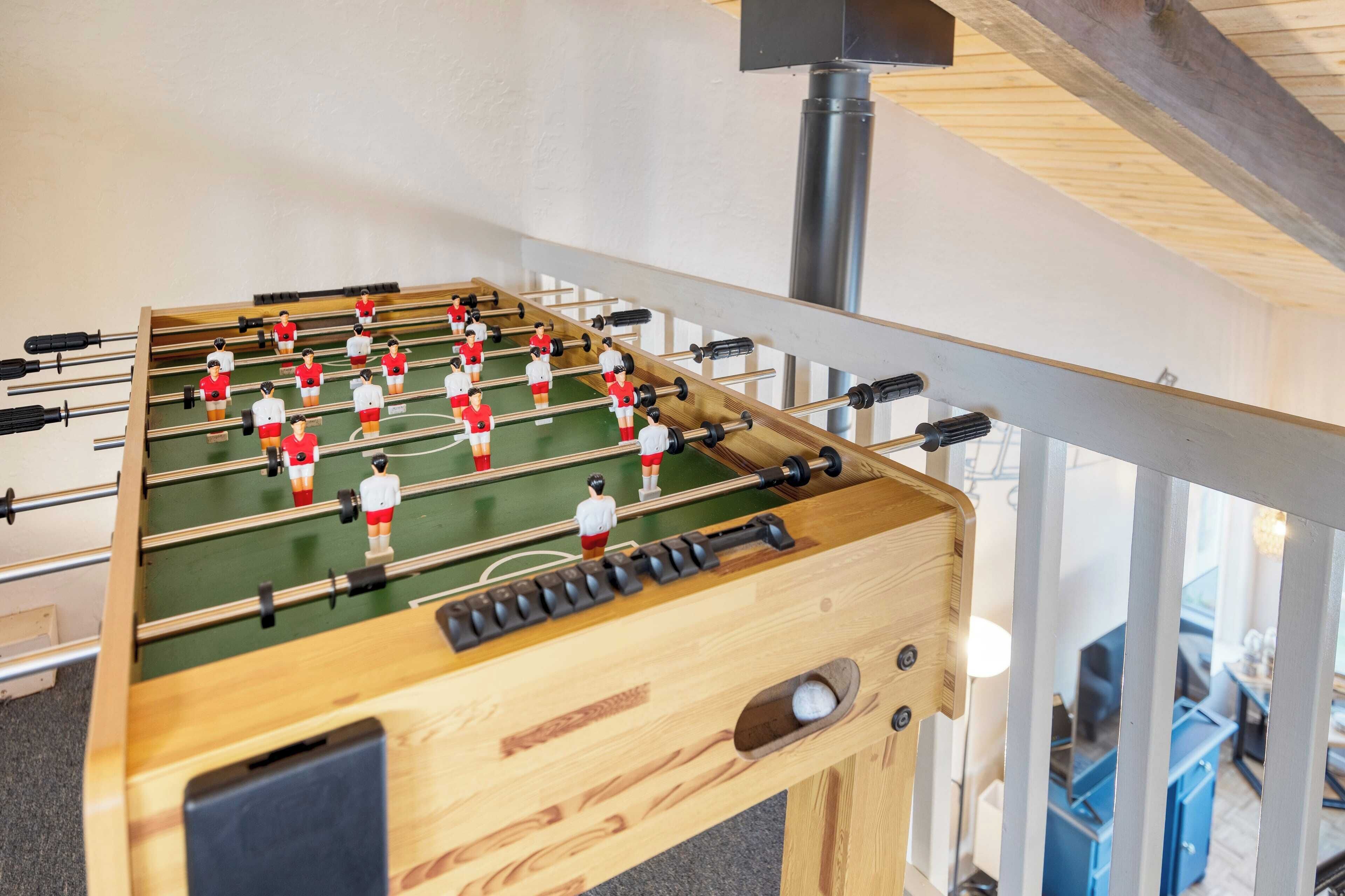 A wooden foosball table with a green playing surface and black rods, located in a room with a wooden ceiling and a metal railing.