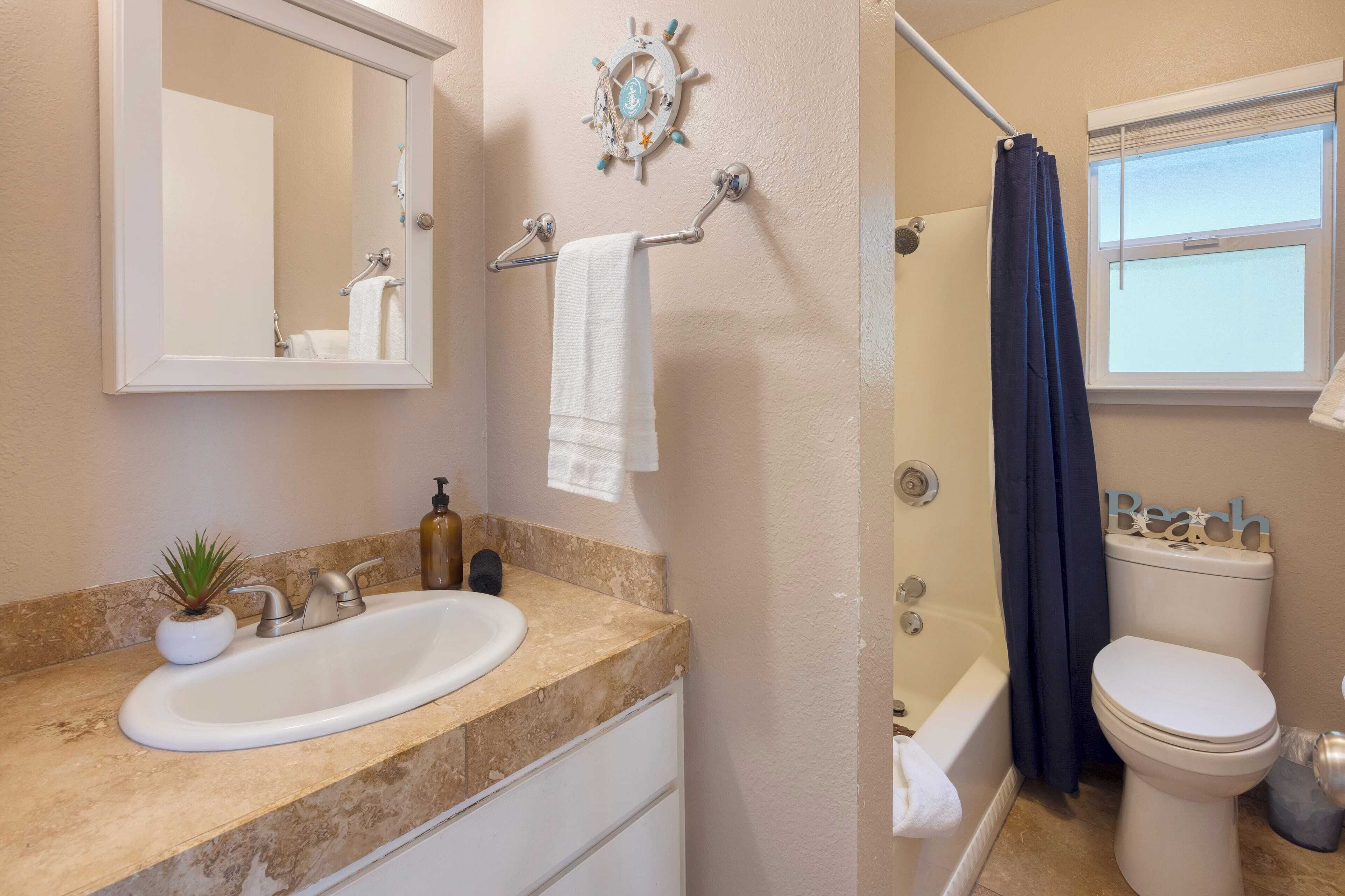 A bathroom with a sink, mirror, towel rack, and a ship's wheel decoration.