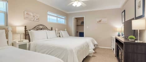 A bedroom with two beds, a ceiling fan, bedside lamps, a dresser, and framed artwork on the walls.