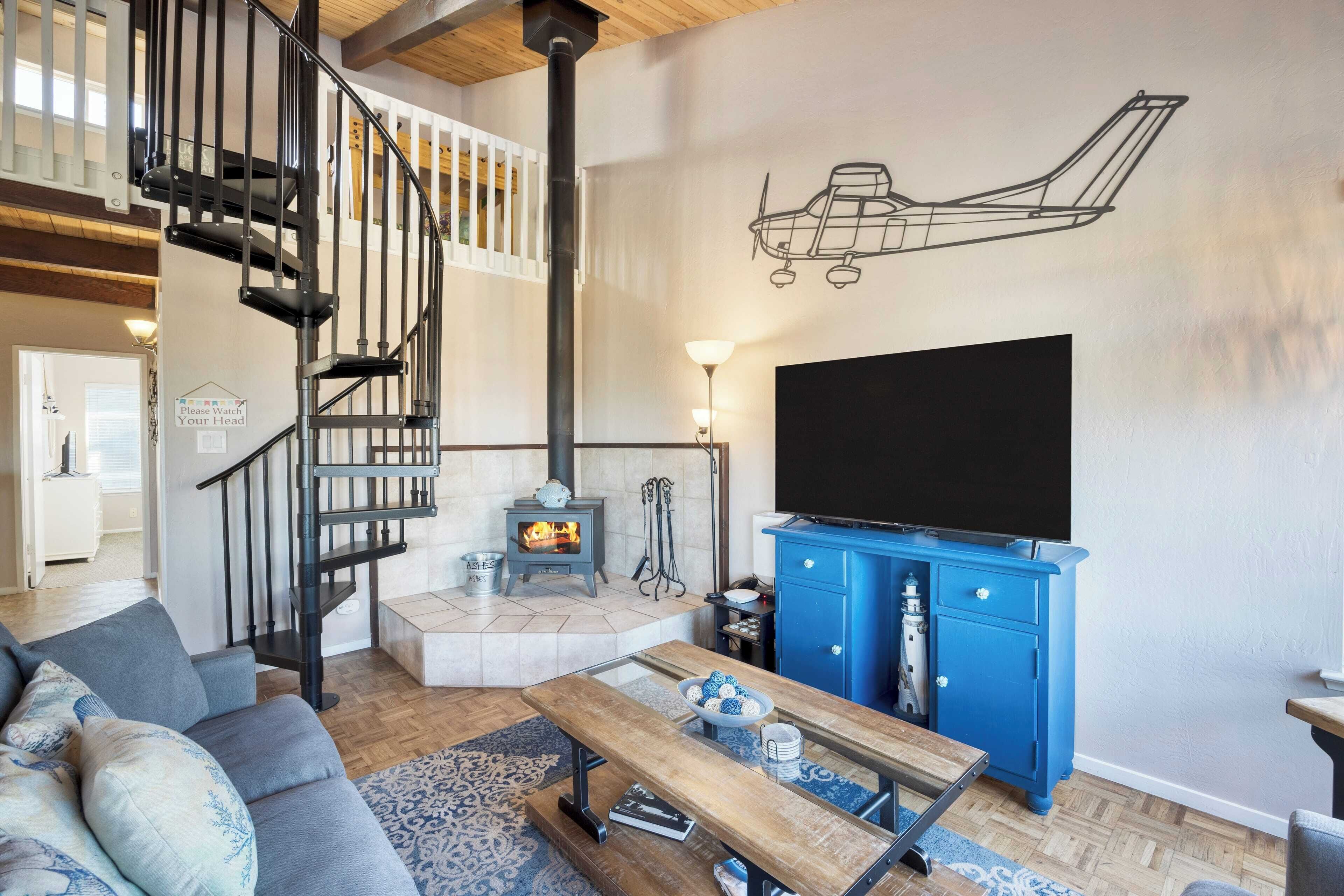 A living room with a staircase, a fireplace, a blue cabinet, and a large TV.