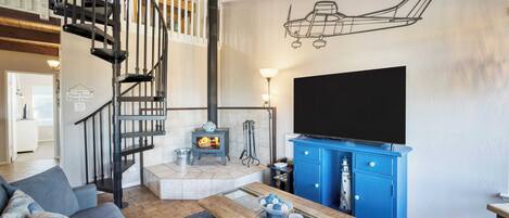 A living room with a staircase, a fireplace, a blue cabinet, and a large TV.