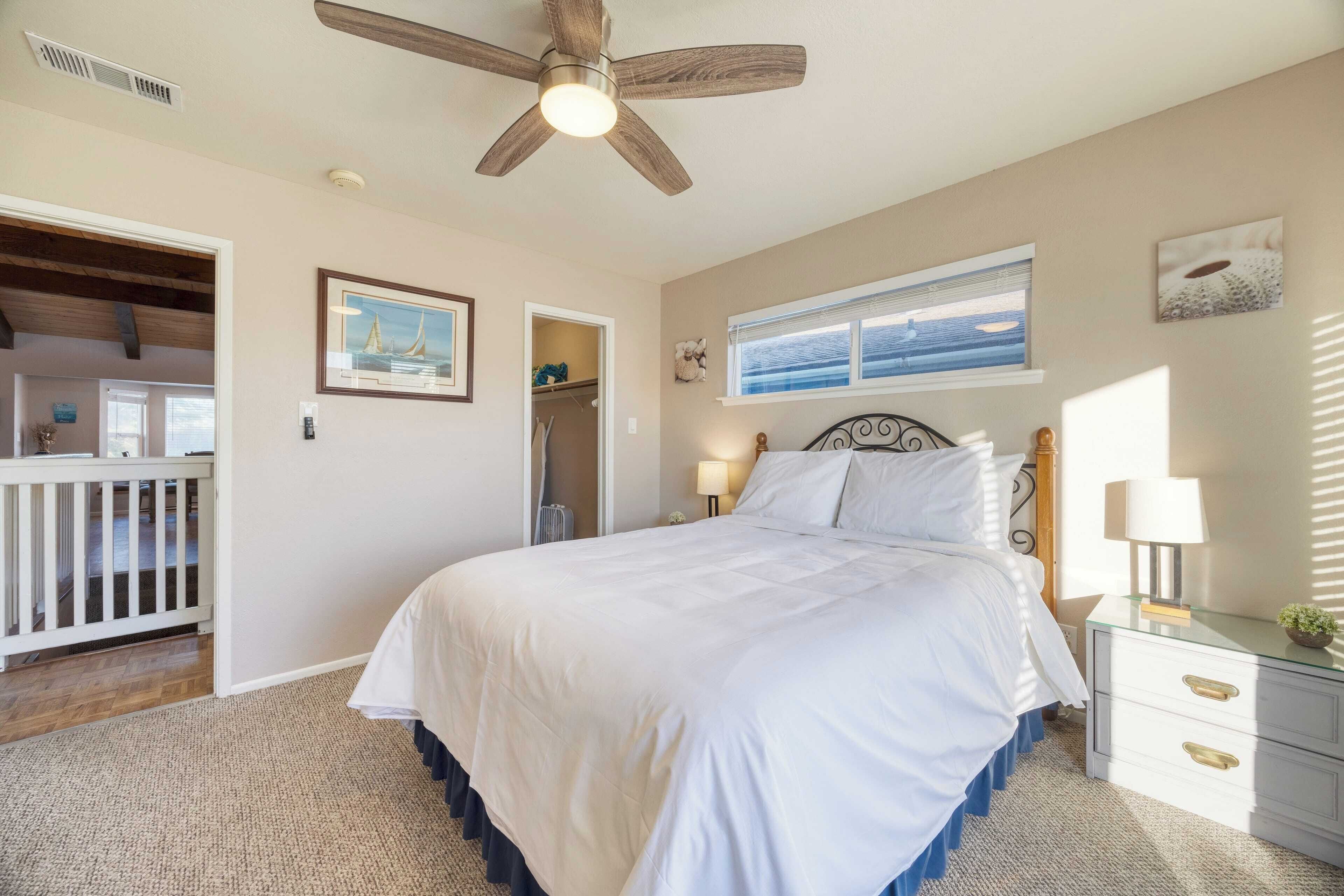 A bedroom with a large bed, a ceiling fan, a window with a view, and a nightstand with a lamp.