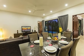 A dining area with a table set for four, a television, and a sofa. - West Facing Boutique Pool Villa Three Bedrooms Villa (Phuket)