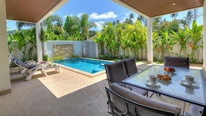 Un espacio al aire libre cubierto con piscina, sillones de descanso y una mesa con vasos y tazones.