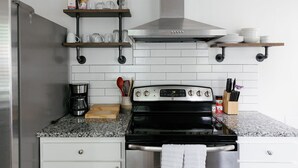 Une cuisine équipée d’une cuisinière en acier inoxydable, de meubles blancs et d’une machine à café.