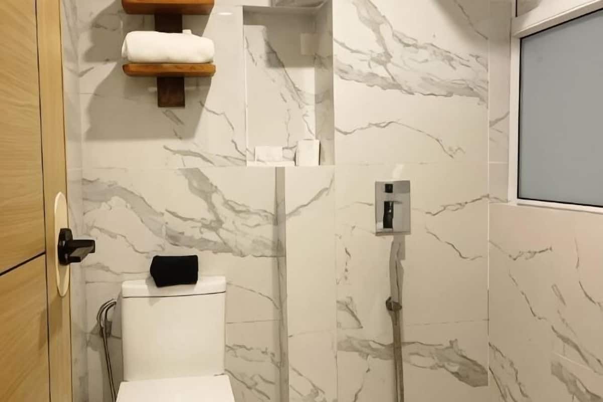 A bathroom with a toilet, a shower, marble walls, and a wooden shelf with towels.