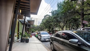 Una calle estrecha con coches aparcados, un edificio con techo inclinado y macetas a lo largo de la acera.