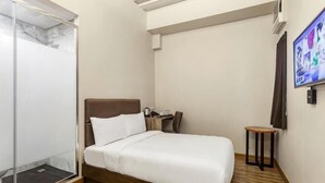 Una habitación de hotel con una cama, una mesita, una silla, un televisor y un armario.