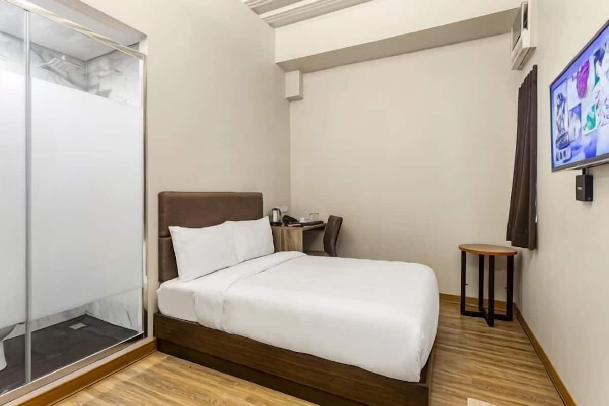 A hotel room with a bed, a small table, a chair, a TV, and a wardrobe.