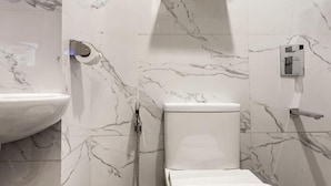 Un baño con pared de mármol, lavamanos, inodoro y ducha.