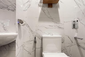 A bathroom with a marble wall, a sink, a toilet, and a shower. - Airo Suites Makati (Makati)