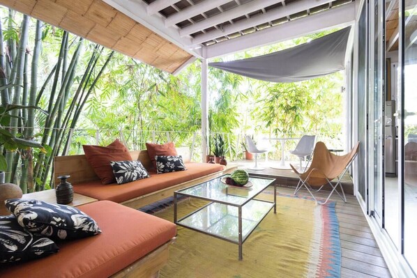 A modern living room with a glass coffee table, orange sofa, and white chairs.