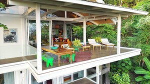 Ein modernes Haus mit einem Glasbalkon, einem Essbereich und einem Wohnzimmer mit einer Couch und Sesseln.