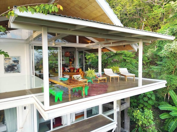 Ein modernes Haus mit einem Glasbalkon, einem Essbereich und einem Wohnzimmer mit einer Couch und Sesseln.