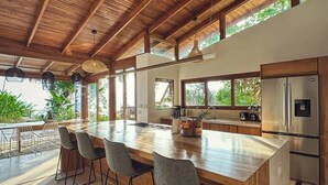 A spacious kitchen with a large island, bar stools, and a stainless steel refrigerator. - Casa Rica _ Stunning Ocean Views and Private Pool (Cóbano)