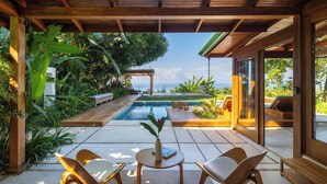 A modern outdoor patio with a pool, wooden furniture, and lush greenery. - Casa Rica _ Stunning Ocean Views and Private Pool (Cóbano)