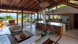 An open-plan living area with a kitchen, dining space, and seating area overlooking a scenic view. - Casa Rica _ Stunning Ocean Views and Private Pool (Cóbano)