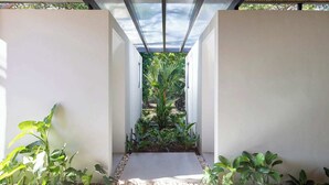 Un corredor moderno de arquitectura con techo de vidrio, rodeado de abundante vegetación y paredes blancas.