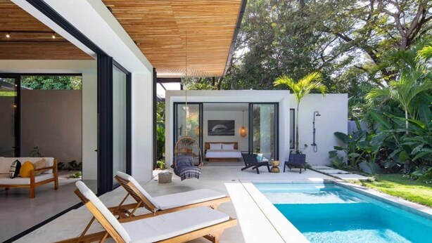 Une maison moderne dotée d’une piscine, d’un patio avec des chaises longues et d’un jardin.