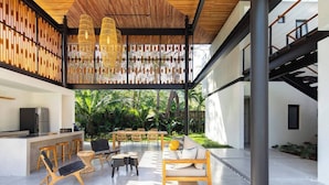 Un espace de vie extérieur moderne comprenant une cuisine, un coin salon et une vue sur une végétation luxuriante.