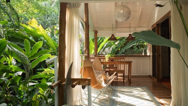 A room with a wooden table and chairs, a hanging light fixture, and a view of lush greenery outside. - Mid Tide Bungalow - Walking distance to the Surf and Restaurants (Santa Teresa Beach)