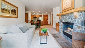 A living room with a fireplace, a sofa, a coffee table with a plant, and a dining area in the background. - Slope-side Condo in Keystone (Keystone)