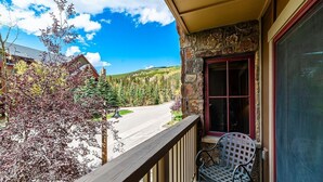 A balcony with a view of a road and trees, a stone wall, and a metal chair. - Slope-side Condo in Keystone (Keystone)