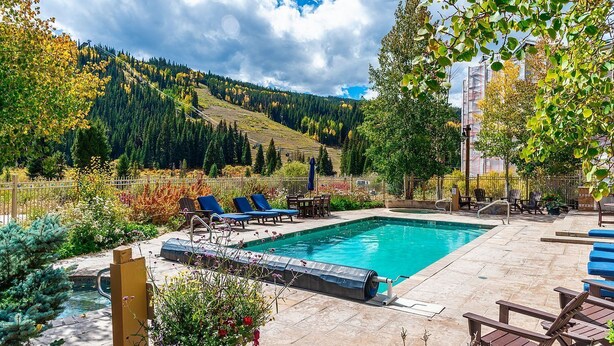 A swimming pool with lounge chairs, surrounded by a garden and a view of a forested hillside. - Slope-side Condo in Keystone (Keystone)