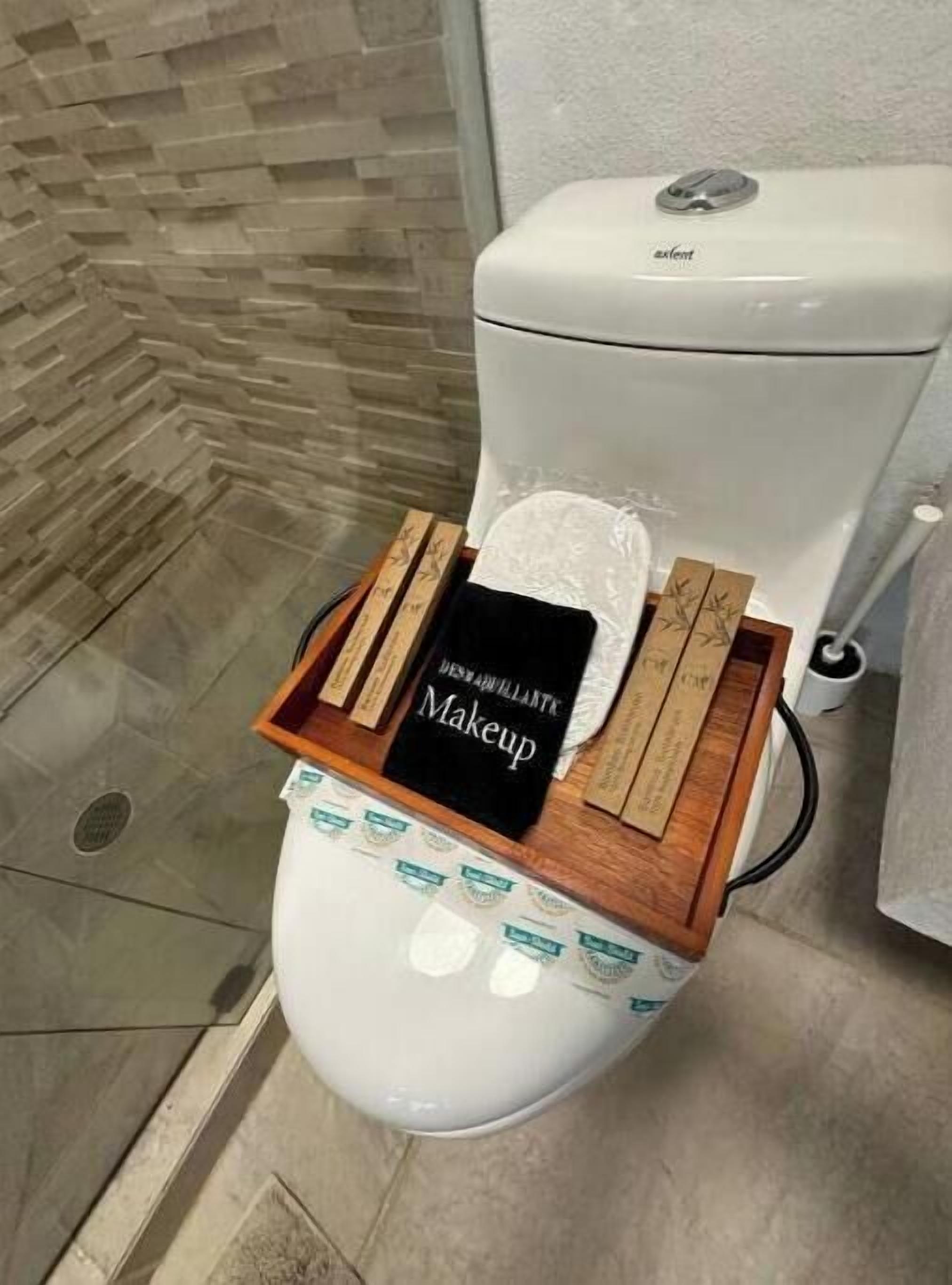 A toilet with a wooden tray holding a book titled 'Makeup' and a tissue box.