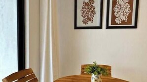 Een houten eettafel met twee stoelen, een potplant en twee kunstwerken met bloemen op de muur.