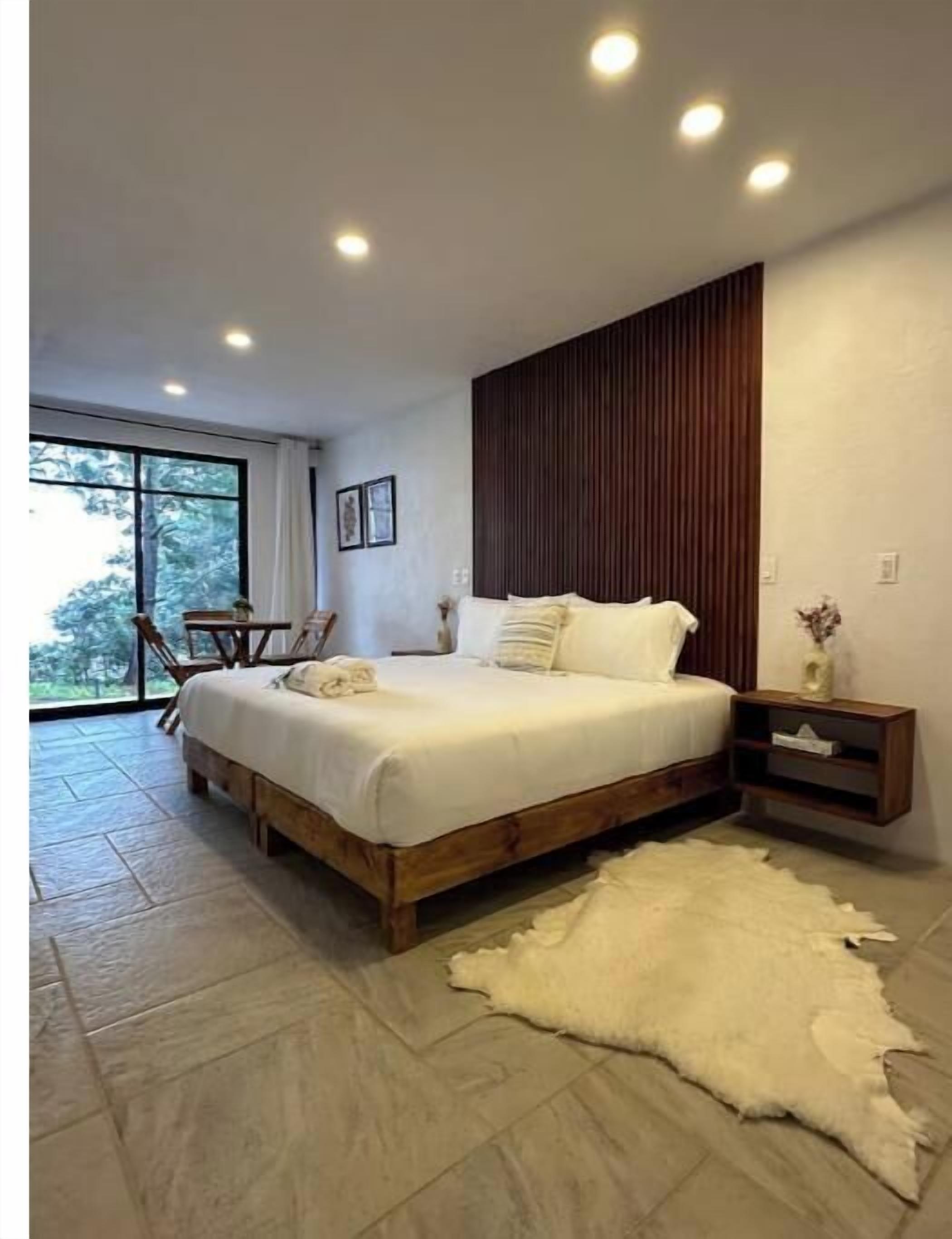 A modern bedroom with a large bed, wooden headboard, and a stone floor.