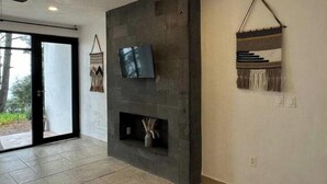 Een moderne woonkamer met een stenen open haard, een flatscreen televisie aan de muur en een geweven wanddecoratie.