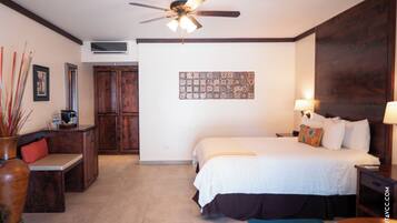 Habitación de hotel con cama, escritorio, silla, ventilador de techo, aire acondicionado de pared y pared decorada con azulejos.