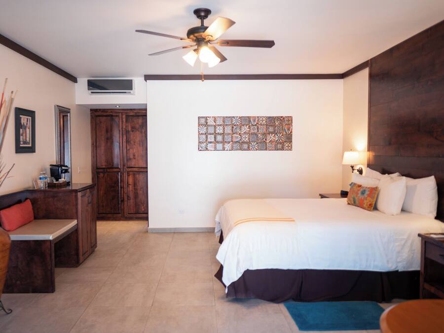 Habitación de hotel con cama, escritorio, silla, ventilador de techo, aire acondicionado de pared y pared decorada con azulejos.