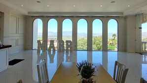 Un comedor amplio con una larga mesa, un candelabro y grandes ventanales que ofrecen vistas al paisaje.