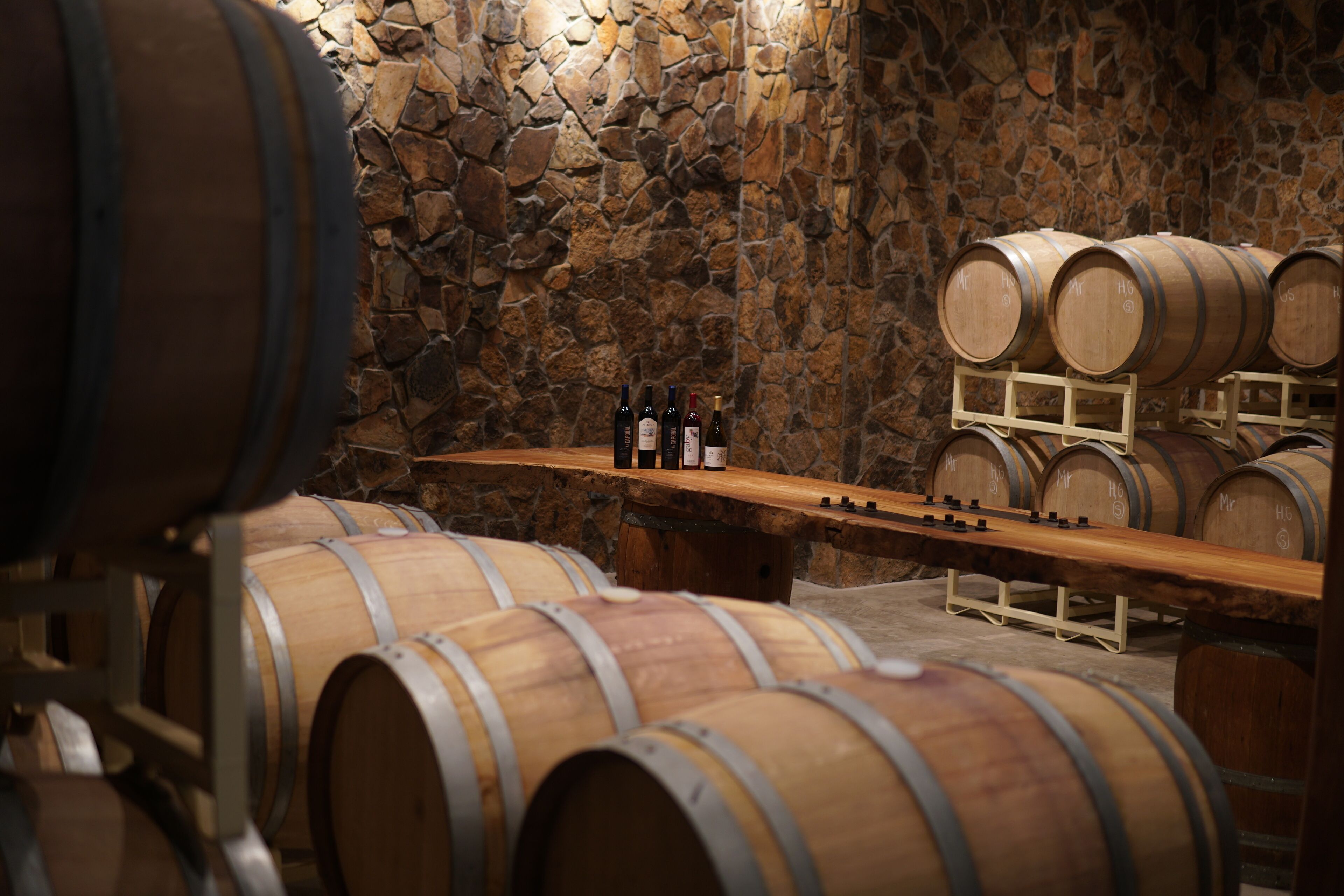 Des barriques en bois, dans une cave dont le mur est en pierre.