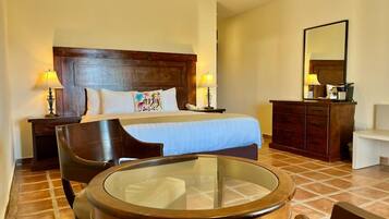Habitación de hotel con una cama, dos mesitas de noche con lámparas, un aparador de madera, una mesa redonda de vidrio y una silla.