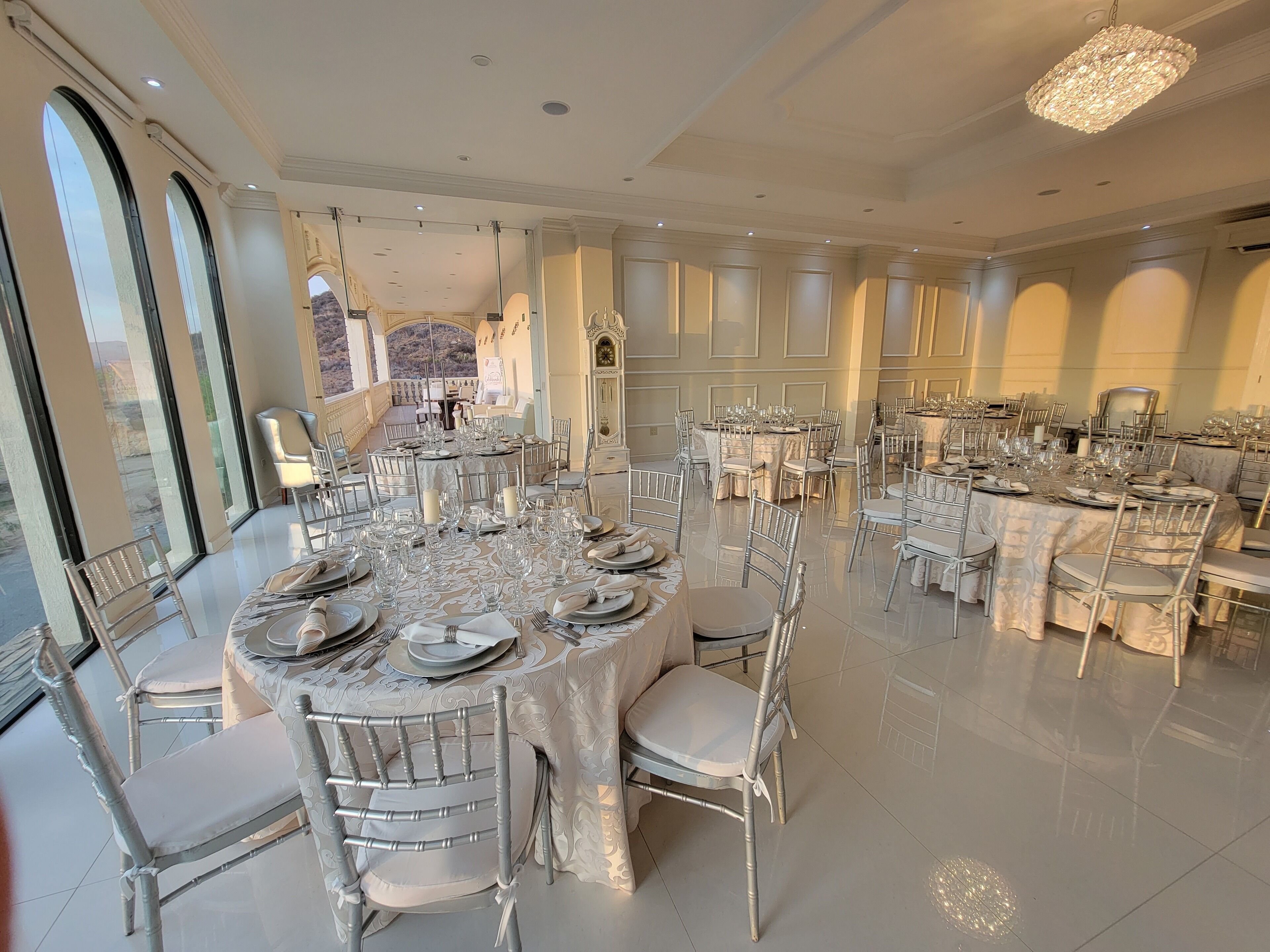 A spacious dining area with round tables, chairs, and a chandelier.