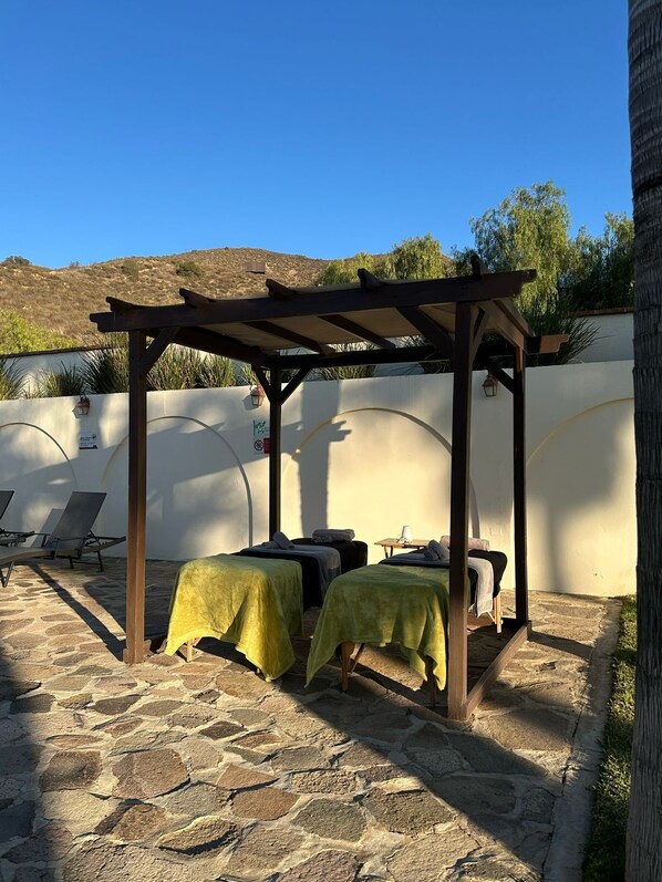 A covered outdoor seating area with two beds, a pergola, and a stone patio. - Hotel Hacienda Guadalupe (Valle de Guadalupe)