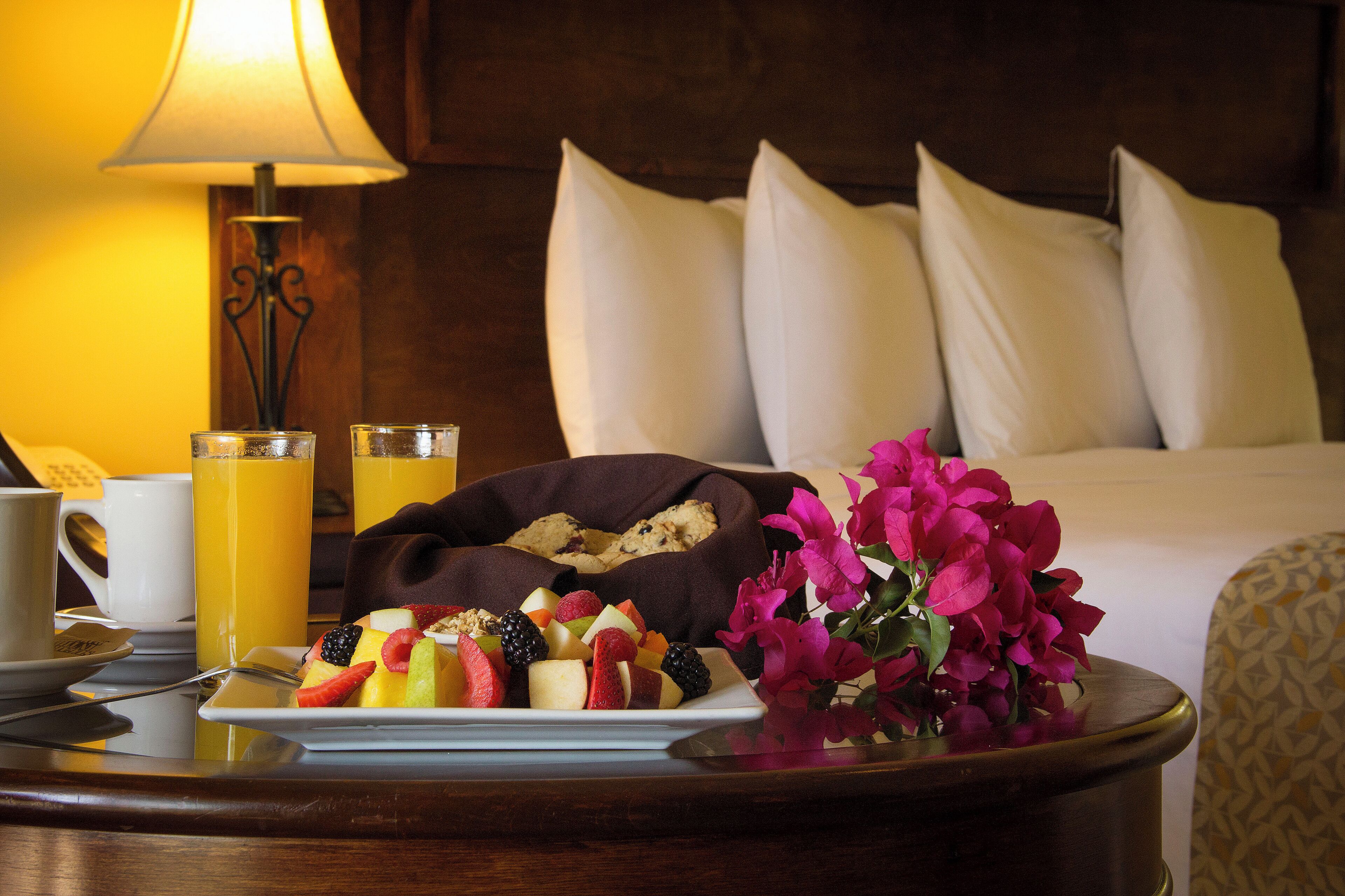 A neatly arranged breakfast table with a plate of fruit, a cookie dish, a glass of orange juice, and a vase of flowers.