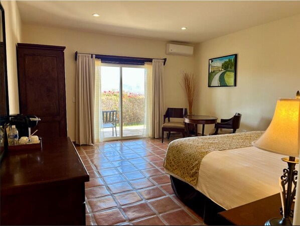 A hotel room with a bed, a desk, a chair, a table, and a view of the outdoors through a sliding door.