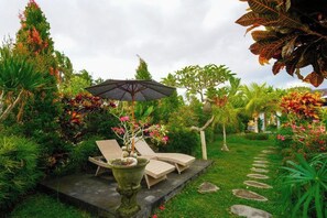 A garden with a stone pathway, a seating area with a table and chairs, and a large umbrella. - Green Coconut Cottage Ubud (Bali)
